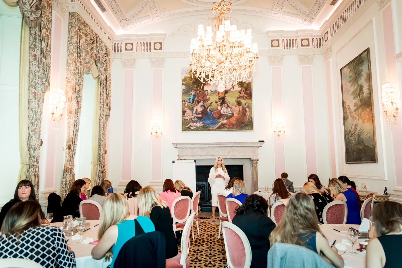 Emily Williams speaking to guests beneath a chandelier in London